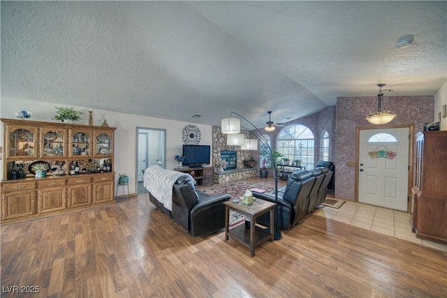 2910 Sunset St, Pahrump, NV 89060 - living area featuring light wood finished floors, a ceiling fan, a textured ceiling, vaulted ceiling, and a stone fireplace