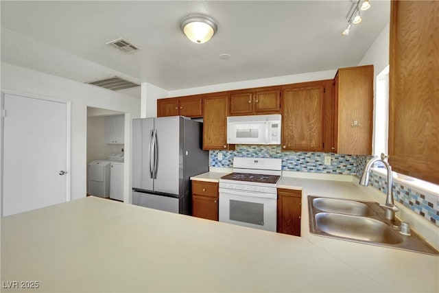 1676 Divinity St, Las Vegas, NV 89142 - kitchen featuring white appliances, washing machine and clothes dryer, tasteful backsplash, light countertops, and brown cabinetry