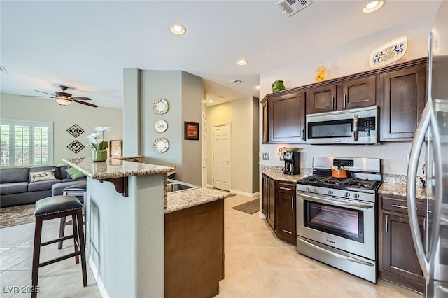 247 Integrity Ridge Dr, Henderson, NV 89052 - kitchen featuring stainless steel appliances, light tile patterned floors, dark brown cabinets, light stone countertops, and a kitchen bar