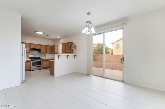 3844 Kit Fox St, Las Vegas, NV 89122 - kitchen featuring gas range, under cabinet range hood, freestanding refrigerator, brown cabinetry, and a chandelier