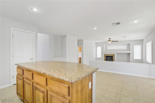 10015 Willowbrook Pond Rd, Las Vegas, NV 89148 - kitchen featuring a ceiling fan, a center island, light stone counters, a fireplace, and light tile patterned floors