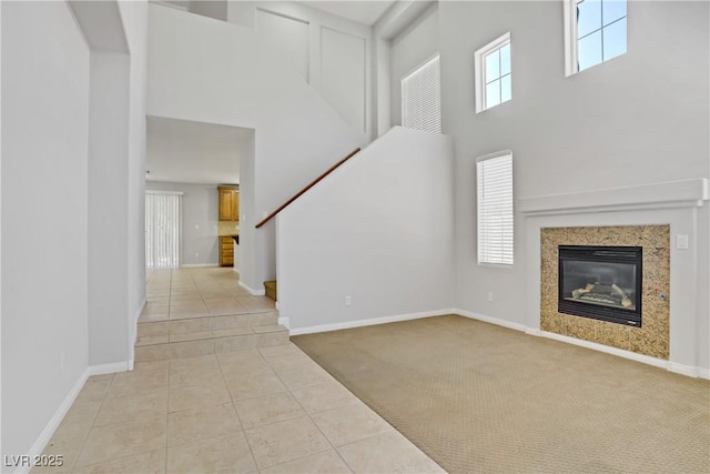 10015 Willowbrook Pond Rd, Las Vegas, NV 89148 - unfurnished living room with a towering ceiling, light colored carpet, light tile patterned floors, stairway, and a glass covered fireplace