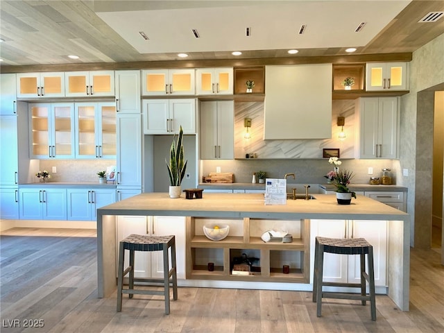 3012 Hawksdale Dr, Las Vegas, NV 89134 - kitchen featuring backsplash, a kitchen island with sink, open shelves, a breakfast bar, and light wood-style floors