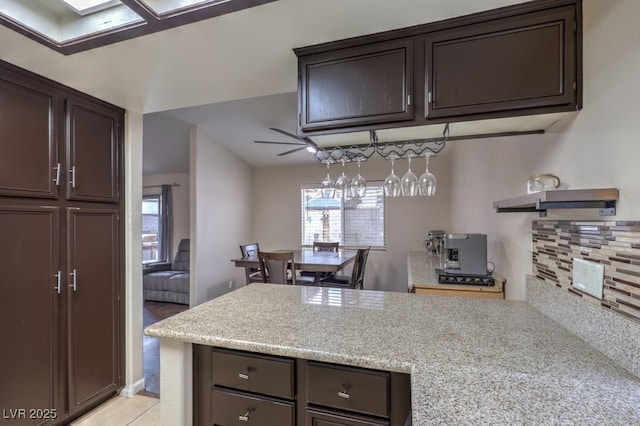 4006 Clove Tree Ct, North Las Vegas, NV 89031 - kitchen featuring dark brown cabinetry, decorative backsplash, a peninsula, and light stone countertops