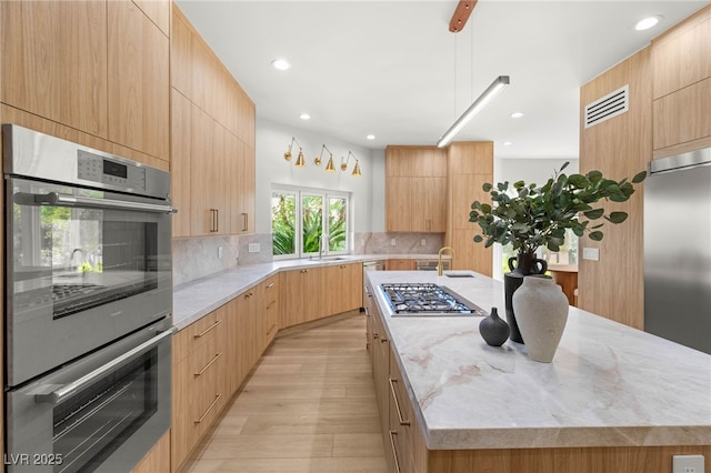 8617 Titleist Cir, Las Vegas, NV 89117 - kitchen with appliances with stainless steel finishes, modern cabinets, a kitchen island with sink, light brown cabinets, and tasteful backsplash