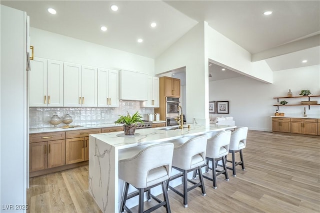 1144 Calico Ridge Dr, Henderson, NV 89011 - kitchen featuring light wood-style floors, a kitchen breakfast bar, light stone counters, tasteful backsplash, and double oven