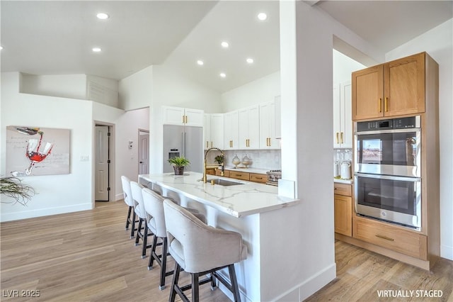 1144 Calico Ridge Dr, Henderson, NV 89011 - kitchen featuring stainless steel appliances, light wood-style floors, a kitchen bar, light stone counters, and high vaulted ceiling