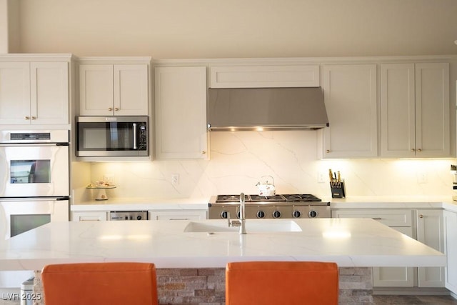 9 Knob Oak Dr, Henderson, NV 89052 - kitchen featuring wall chimney range hood, white double oven, stainless steel microwave, an island with sink, and white cabinets