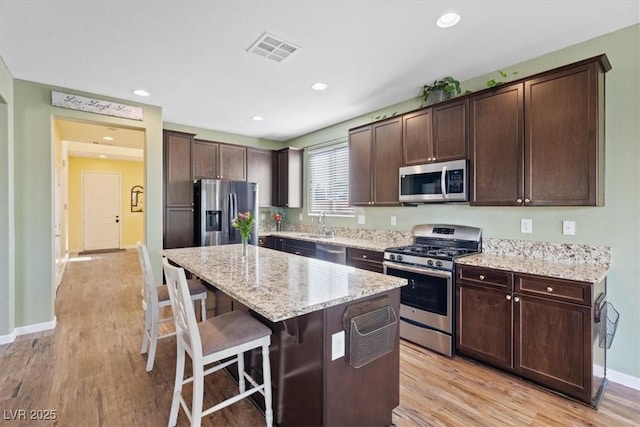 9305 Briar Bridge Ave, Las Vegas, NV 89148 - kitchen with appliances with stainless steel finishes, a breakfast bar area, dark brown cabinetry, a kitchen island, and light wood-style flooring