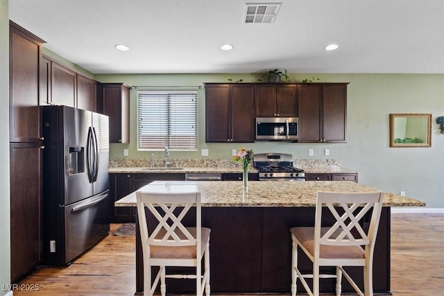 9305 Briar Bridge Ave, Las Vegas, NV 89148 - kitchen with stainless steel appliances, dark brown cabinets, a kitchen bar, light wood-style flooring, and a center island