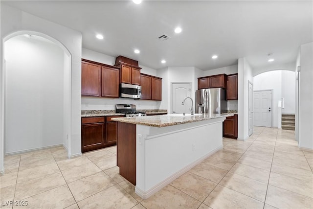 9217 Apollo Heights Ave, Las Vegas, NV 89149 - kitchen featuring appliances with stainless steel finishes, arched walkways, light stone countertops, a kitchen island with sink, and light tile patterned floors