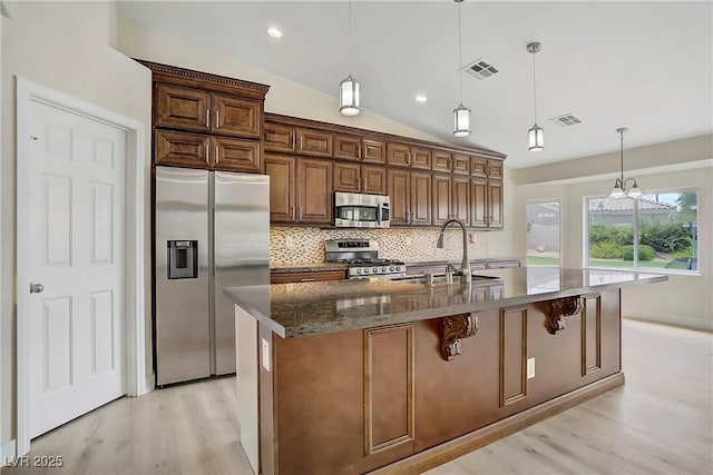 6125 Resort Ridge St, Las Vegas, NV 89130 - kitchen with appliances with stainless steel finishes, light wood-type flooring, tasteful backsplash, a center island with sink, and dark stone counters