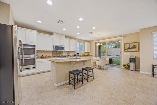 1084 Via Della Costrella, Henderson, NV 89011 - kitchen featuring stainless steel appliances, white cabinetry, recessed lighting, light stone countertops, and a kitchen bar