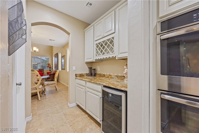 1084 Via Della Costrella, Henderson, NV 89011 - indoor dry bar with beverage cooler, stainless steel double oven, arched walkways, light tile patterned floors, and a chandelier