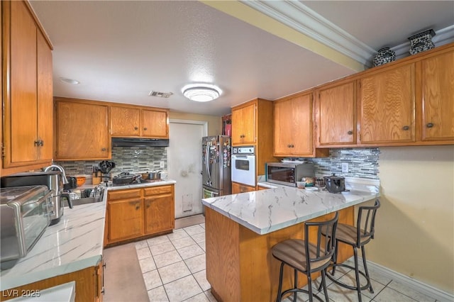 111 Narcissus Ln, Las Vegas, NV 89107 - kitchen featuring appliances with stainless steel finishes, a peninsula, brown cabinets, backsplash, and crown molding