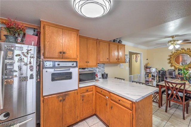 111 Narcissus Ln, Las Vegas, NV 89107 - kitchen with appliances with stainless steel finishes, a peninsula, light tile patterned floors, light countertops, and ornamental molding