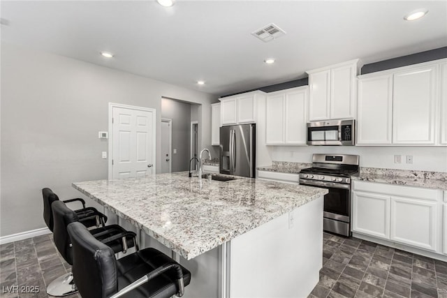 7615 Quail Dust St, North Las Vegas, NV 89084 - kitchen with appliances with stainless steel finishes, a kitchen island with sink, white cabinetry, light stone countertops, and recessed lighting