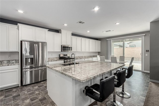 7615 Quail Dust St, North Las Vegas, NV 89084 - kitchen with stainless steel appliances, white cabinetry, light stone countertops, a breakfast bar area, and an island with sink
