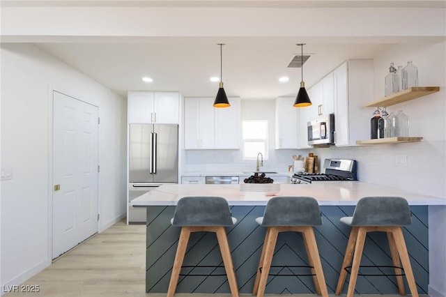 119 Cedar St, Henderson, NV 89015 - kitchen featuring stainless steel appliances, a peninsula, open shelves, white cabinetry, and a breakfast bar