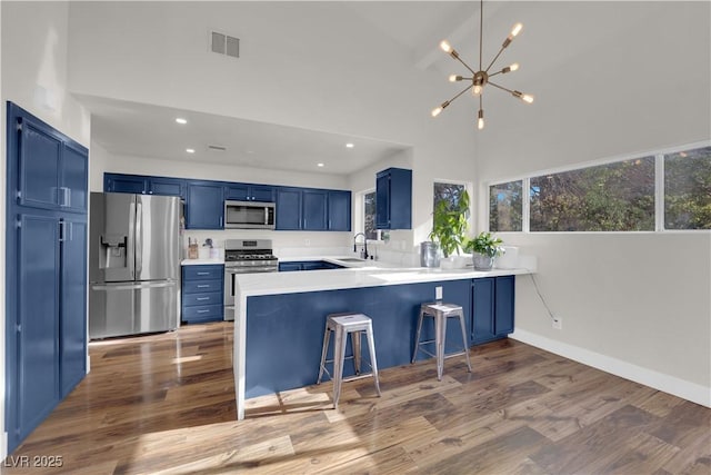 9089 Harvest Season Ct, Henderson, NV 89074 - kitchen featuring appliances with stainless steel finishes, blue cabinetry, a peninsula, wood finished floors, and recessed lighting