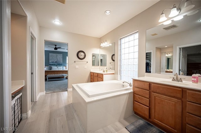 6937 Puetollano Dr, North Las Vegas, NV 89084 - ensuite bathroom featuring a bath, two vanities, a ceiling fan, wood finished floors, and a spacious closet