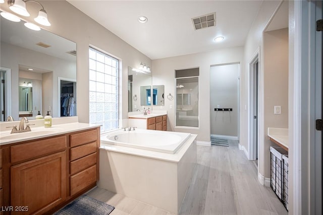 6937 Puetollano Dr, North Las Vegas, NV 89084 - full bathroom with a garden tub, a stall shower, two vanities, a walk in closet, and wood finished floors