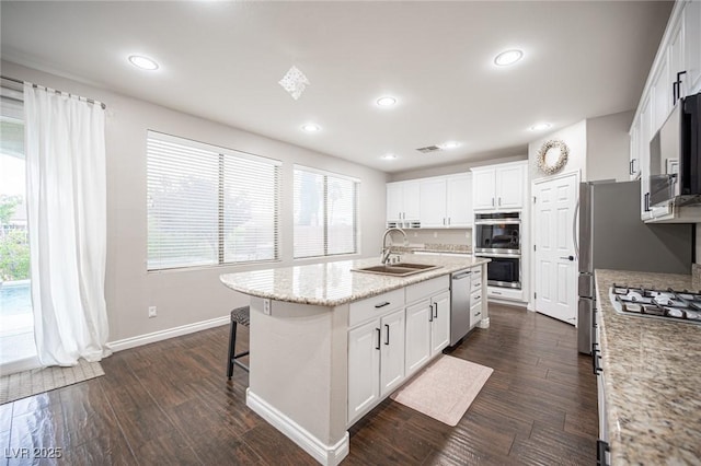 6937 Puetollano Dr, North Las Vegas, NV 89084 - kitchen with appliances with stainless steel finishes, a kitchen island with sink, white cabinets, a kitchen breakfast bar, and dark wood-style flooring