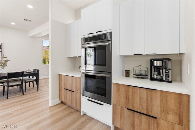 10707 Sleepy Mist Ct, Las Vegas, NV 89141 - kitchen with stainless steel double oven, modern cabinets, light countertops, light wood-type flooring, and white cabinets