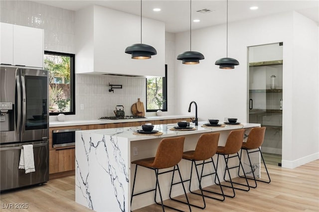 10707 Sleepy Mist Ct, Las Vegas, NV 89141 - kitchen featuring appliances with stainless steel finishes, decorative backsplash, white cabinetry, light wood finished floors, and a breakfast bar