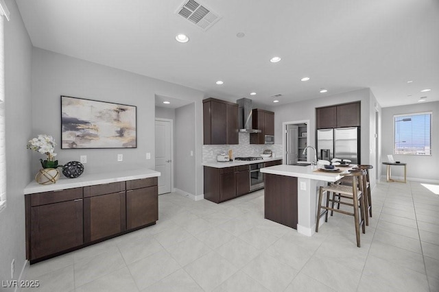 635 Pyrite Will St, Las Vegas, NV 89138 - kitchen with appliances with stainless steel finishes, wall chimney exhaust hood, light countertops, a breakfast bar, and decorative backsplash