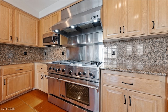 9208 Brilliant Ore Dr, Las Vegas, NV 89143 - kitchen featuring appliances with stainless steel finishes, light brown cabinetry, wall chimney exhaust hood, and dark stone counters