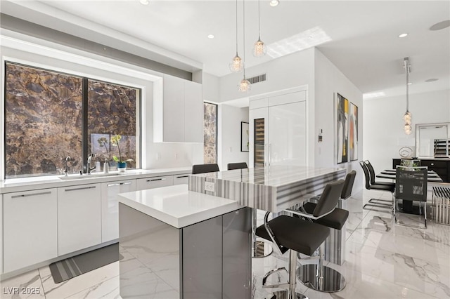 426 Tranquil Peak Ct, Henderson, NV 89012 - kitchen featuring modern cabinets, a center island, white cabinets, hanging light fixtures, and light marble finish flooring