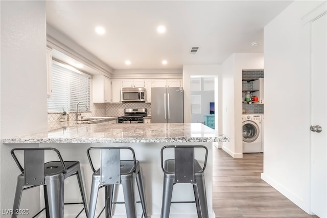 77 Huntfield Dr, Henderson, NV 89074 - kitchen featuring appliances with stainless steel finishes, washer / clothes dryer, a peninsula, a kitchen breakfast bar, and recessed lighting