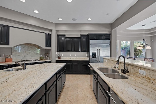 3668 Hillary Elan Ct, Las Vegas, NV 89139 - kitchen with dark cabinetry, stainless steel built in fridge, light stone countertops, light tile patterned floors, and hanging light fixtures