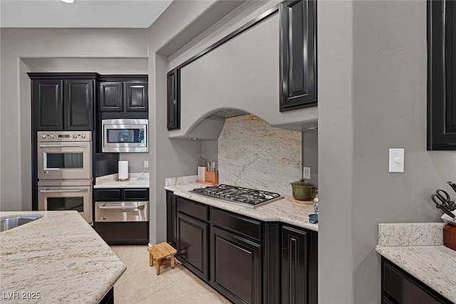 3668 Hillary Elan Ct, Las Vegas, NV 89139 - kitchen with stainless steel appliances, a warming drawer, dark cabinetry, light tile patterned floors, and light stone counters