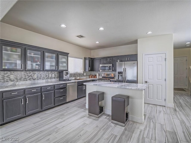7375 Emerald Glow St, Las Vegas, NV 89123 - kitchen featuring stainless steel appliances, wood finish floors, tasteful backsplash, a center island, and light stone countertops
