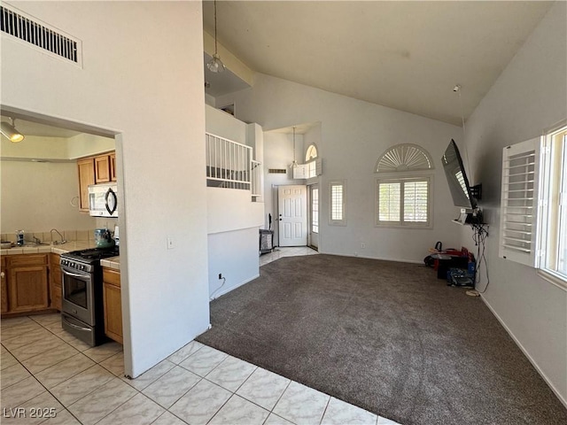 6492 Silent Pine Ave, Las Vegas, NV 89156 - kitchen with stainless steel appliances, high vaulted ceiling, tile countertops, brown cabinetry, and light carpet
