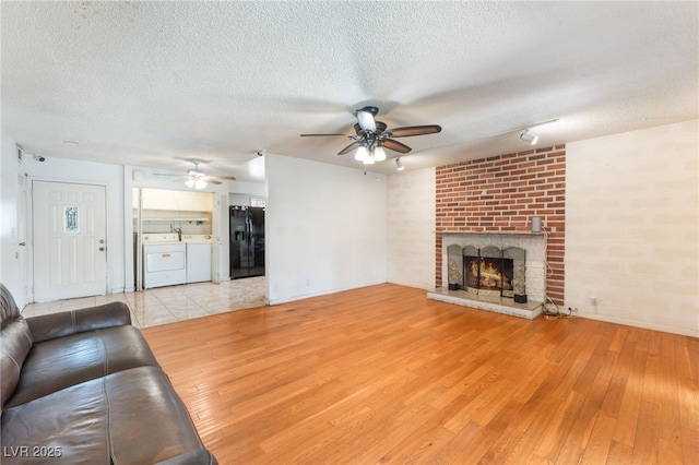 4436 E Ogden Ave, Las Vegas, NV 89110 - unfurnished living room featuring ceiling fan, light wood-style floors, a textured ceiling, a brick fireplace, and washing machine and clothes dryer