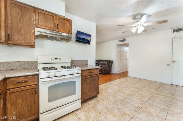 4436 E Ogden Ave, Las Vegas, NV 89110 - kitchen with white gas range, under cabinet range hood, a ceiling fan, brown cabinets, and light countertops