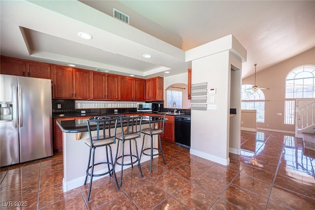 8708 Western Saddle Ave, Las Vegas, NV 89129 - kitchen with stainless steel appliances, dark countertops, a tray ceiling, a breakfast bar, and a kitchen island