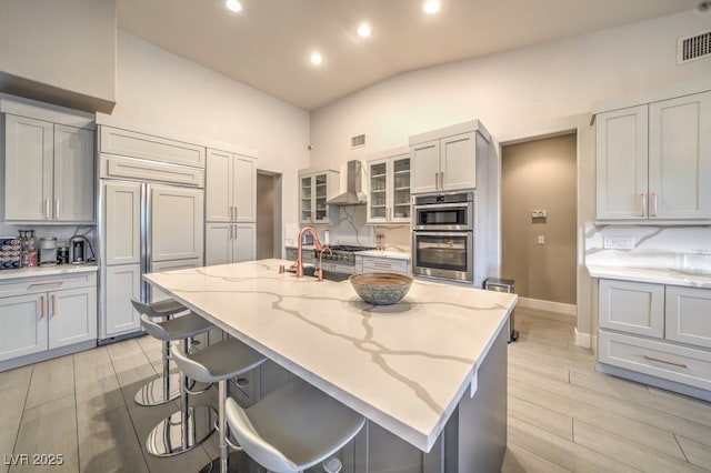 1131 Magic Meadow St, Henderson, NV 89052 - kitchen featuring wall chimney range hood, stainless steel double oven, paneled fridge, light stone counters, and wood tiled floors
