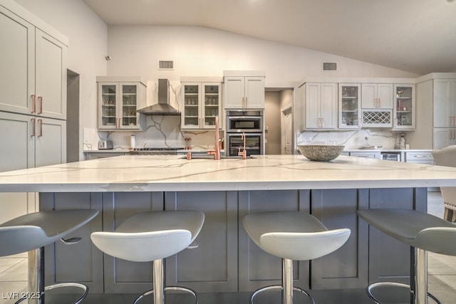 1131 Magic Meadow St, Henderson, NV 89052 - kitchen with wall chimney exhaust hood, lofted ceiling, decorative backsplash, stainless steel appliances, and light stone counters