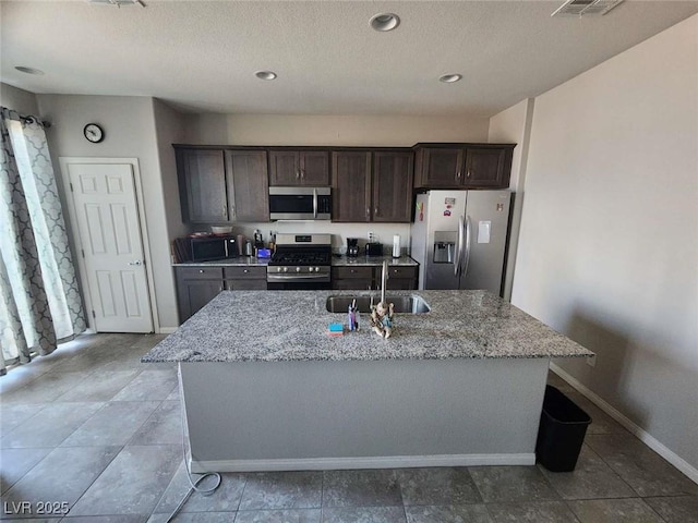 2682 Chinaberry Hill St, Laughlin, NV 89029 - kitchen with stainless steel appliances, dark brown cabinets, a center island with sink, light stone countertops, and a textured ceiling