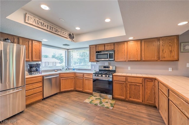 1605 Siboney Dr, Las Vegas, NV 89123 - kitchen featuring stainless steel appliances, tile counters, wood finished floors, brown cabinets, and recessed lighting