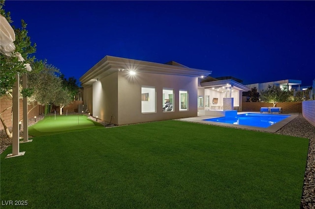 11 Hawkeye Ln, Las Vegas, NV 89135 - back of house at night with an area to practice putting, stucco siding, and a fenced backyard