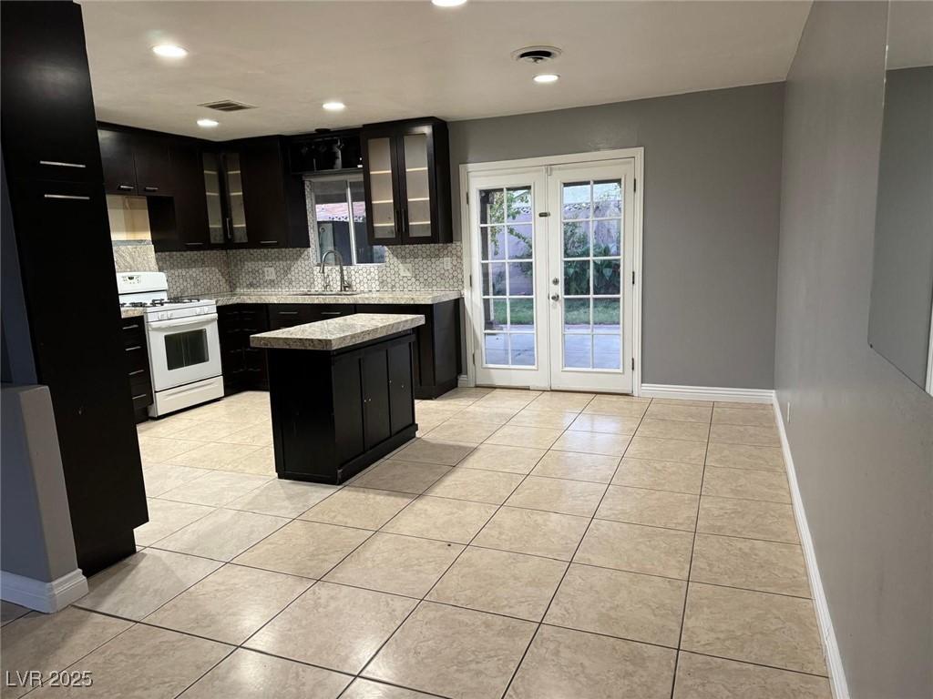 4989 Via De Palma Dr, Las Vegas, NV 89146 - kitchen featuring white range with gas cooktop, dark cabinets, tasteful backsplash, light tile patterned flooring, and recessed lighting