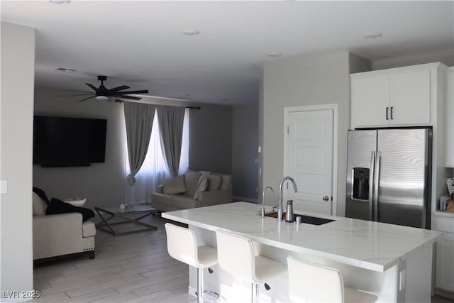 7022 Judith River St, North Las Vegas, NV 89084 - kitchen featuring stainless steel refrigerator with ice dispenser, open floor plan, a center island with sink, light stone countertops, and light wood finished floors