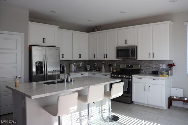 7022 Judith River St, North Las Vegas, NV 89084 - kitchen featuring appliances with stainless steel finishes, tasteful backsplash, a kitchen island with sink, white cabinets, and light stone counters