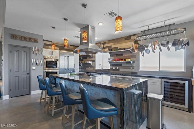 10596 Refugio St, Las Vegas, NV 89141 - kitchen with wine cooler, island exhaust hood, finished concrete flooring, appliances with stainless steel finishes, and a center island