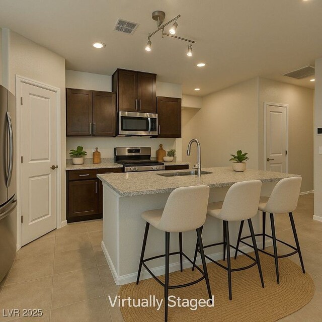 4441 Glossier Ave, North Las Vegas, NV 89084 - kitchen with appliances with stainless steel finishes, a breakfast bar area, light tile patterned floors, dark brown cabinetry, and an island with sink